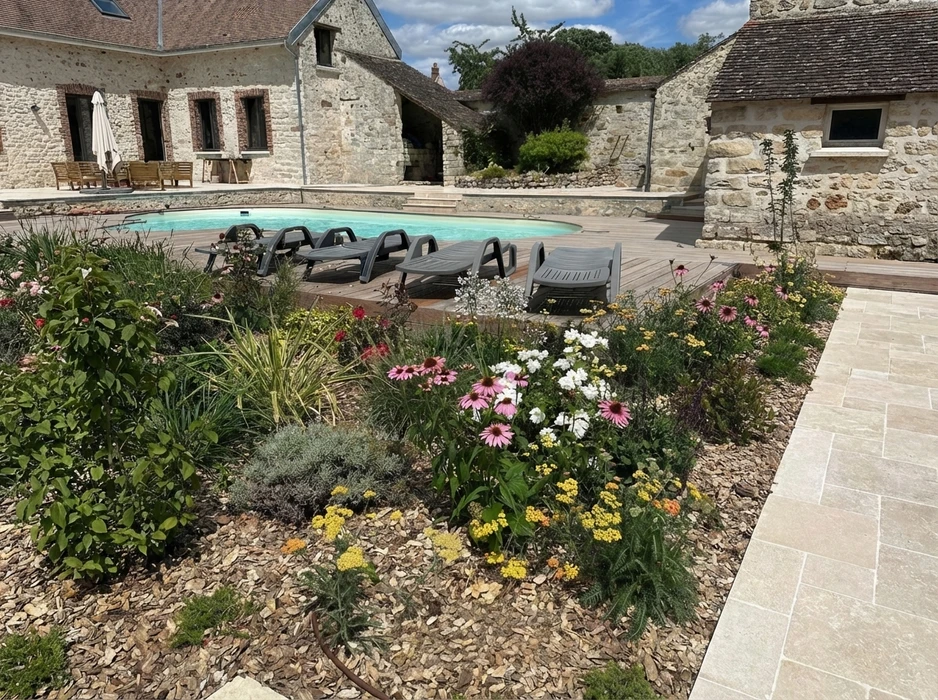Jardin méditerranéen avec massif fleuri en premier plan : échinacées roses, achillées jaunes, gypsophile blanc, lavande coton argentée, sur paillage minéral