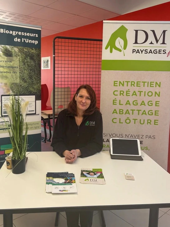 Femme paysagiste concentrée, penchée sur une table de travail, tenant un stylet dans une main et des plans d'aménagement de jardins colorés devant elle. Sur la table, tablette graphique affichant une modélisation 3D d'un projet paysager, papiers techniques avec annotations, boîte de stylos et crayons de couleur. À proximité, un collègue homme consultant les mêmes plans. Lumière naturelle professionnelle, cadre de bureau moderne minimaliste, arrière-plan flou avec écrans d'ordinateur. Image qui capture l'expertise, la collaboration et les outils techniques du bureau d'étude paysager.