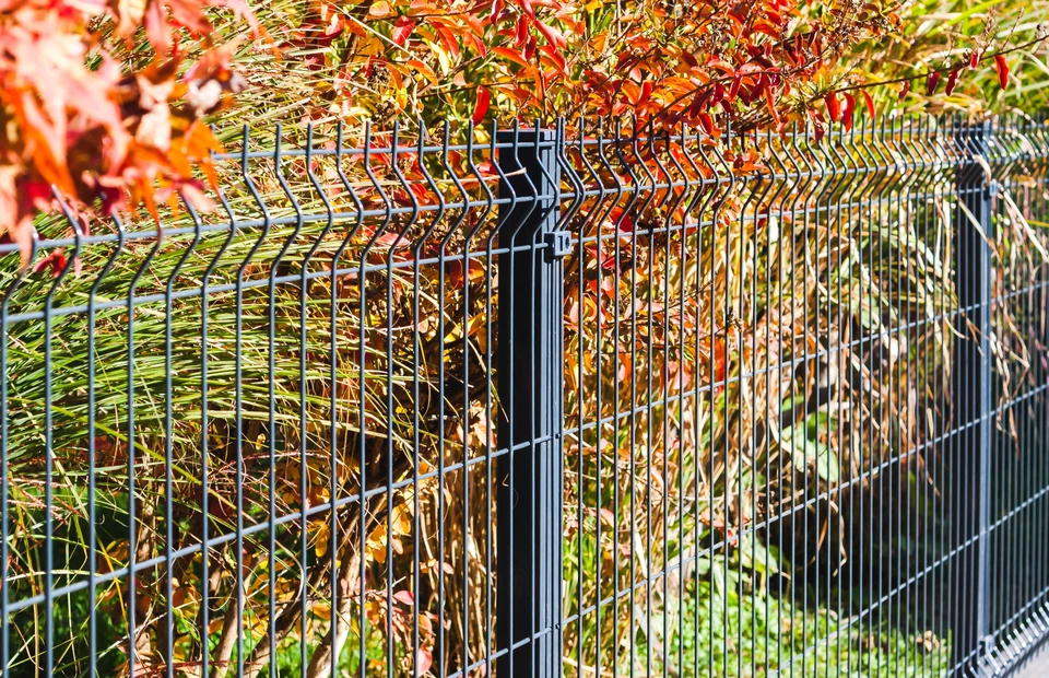 Propriété résidentielle contemporaine avec une clôture aluminium gris anthracite aux lames horizontales, installée sur muret béton blanc. La clôture est intégrée harmonieusement dans un jardin paysagé : pelouse tondue soignée, massifs fleuris variés, arbustes persistants taillés. Au premier plan visible, détail de la clôture montrant sa structure rigide, ses joints réguliers et sa finition lisse. À l'arrière-plan, maison pavillonnaire avec jardin verdoyant. Cadrage permettant de voir à la fois le détail technique de la clôture et son intégration dans l'aménagement global. Lumière naturelle claire, ciel bleu. Style professionnel, photo réaliste de qualité.